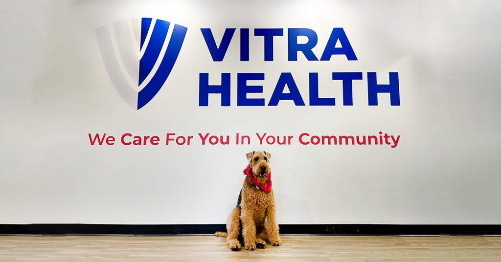 Dog sitting in front of Vitra Health sign