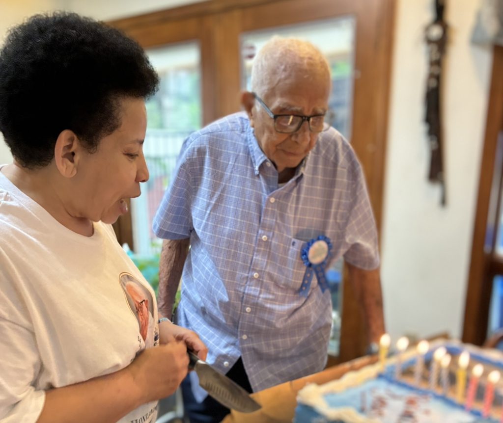 Jose looks lovingly at his birthday cake alongside his daughter and caregiver.
